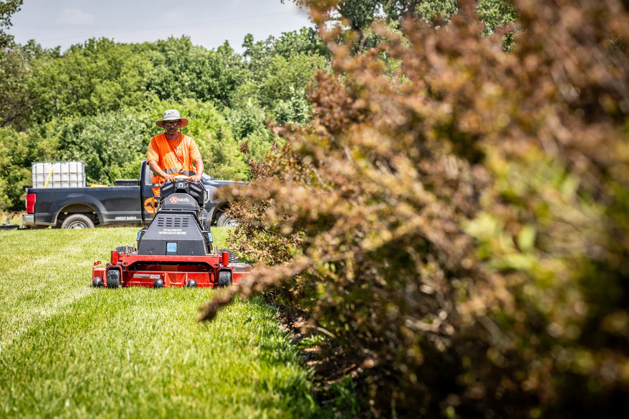 Exmark Turf Tracer Autonomous Series Walk Behind Lawn Mower Tta749Akc604N0 Man Mowing Bushes Wide Angle product image