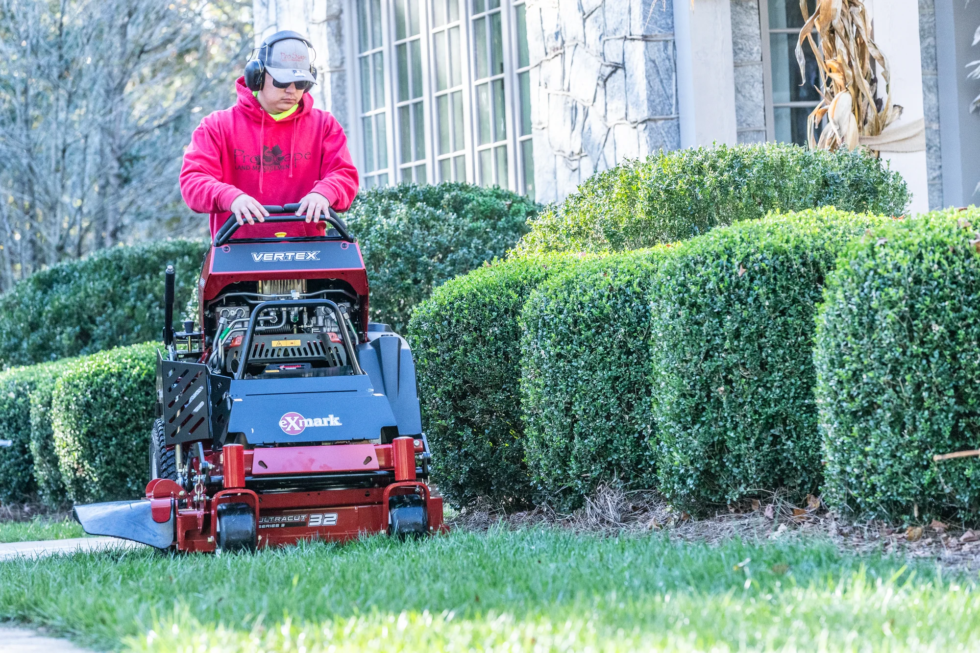 Exmark Vertex E Series Stand On Lawn Mower Vxe600Gka32300 Landscaper Mowing Near Hedges Front View product image