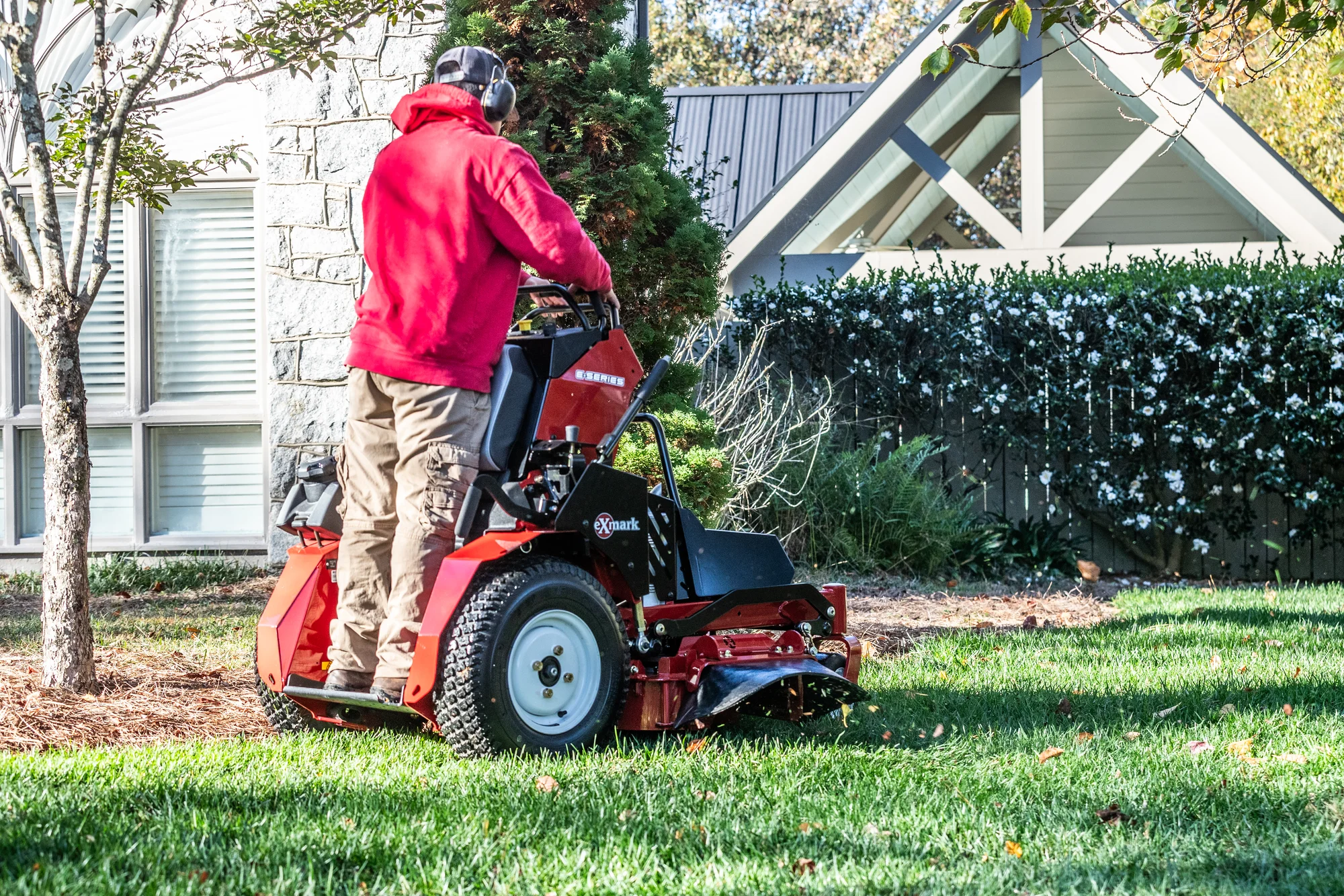 Exmark Vertex E Series Stand-On Lawn Mower VXE600GKA36300 Exmark Vertex E Series Stand On Lawn Mower Vxe600Gka36300 Landscaper Mowing Near Hedges Back View product image