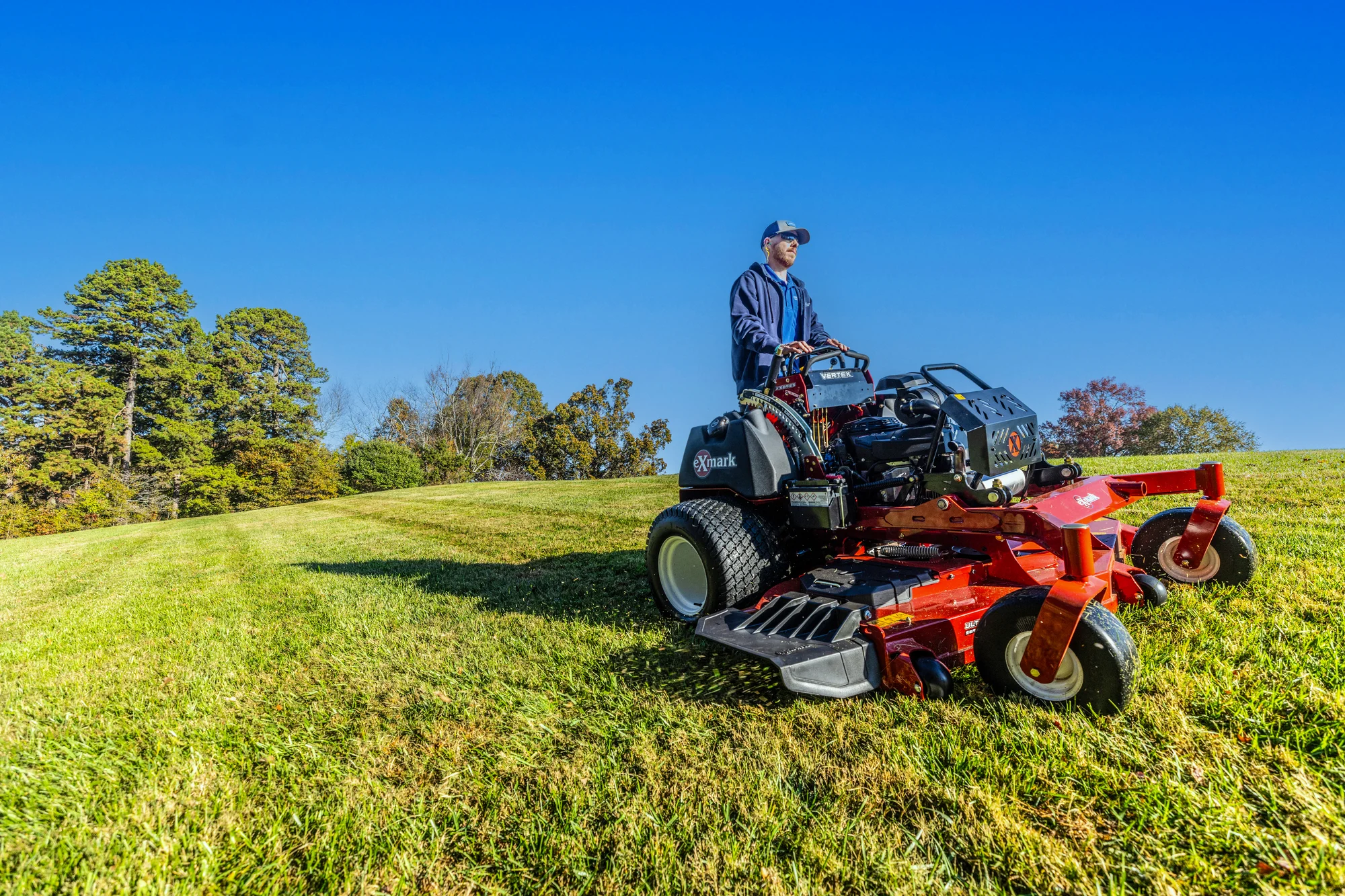 Exmark Vertex X Series Stand-On Lawn Mower VXX999EKA52600 Exmark Vertex X Series Stand On Lawn Mower Vxx999Eka52600 Wide Angle Man Mowing Hill product image