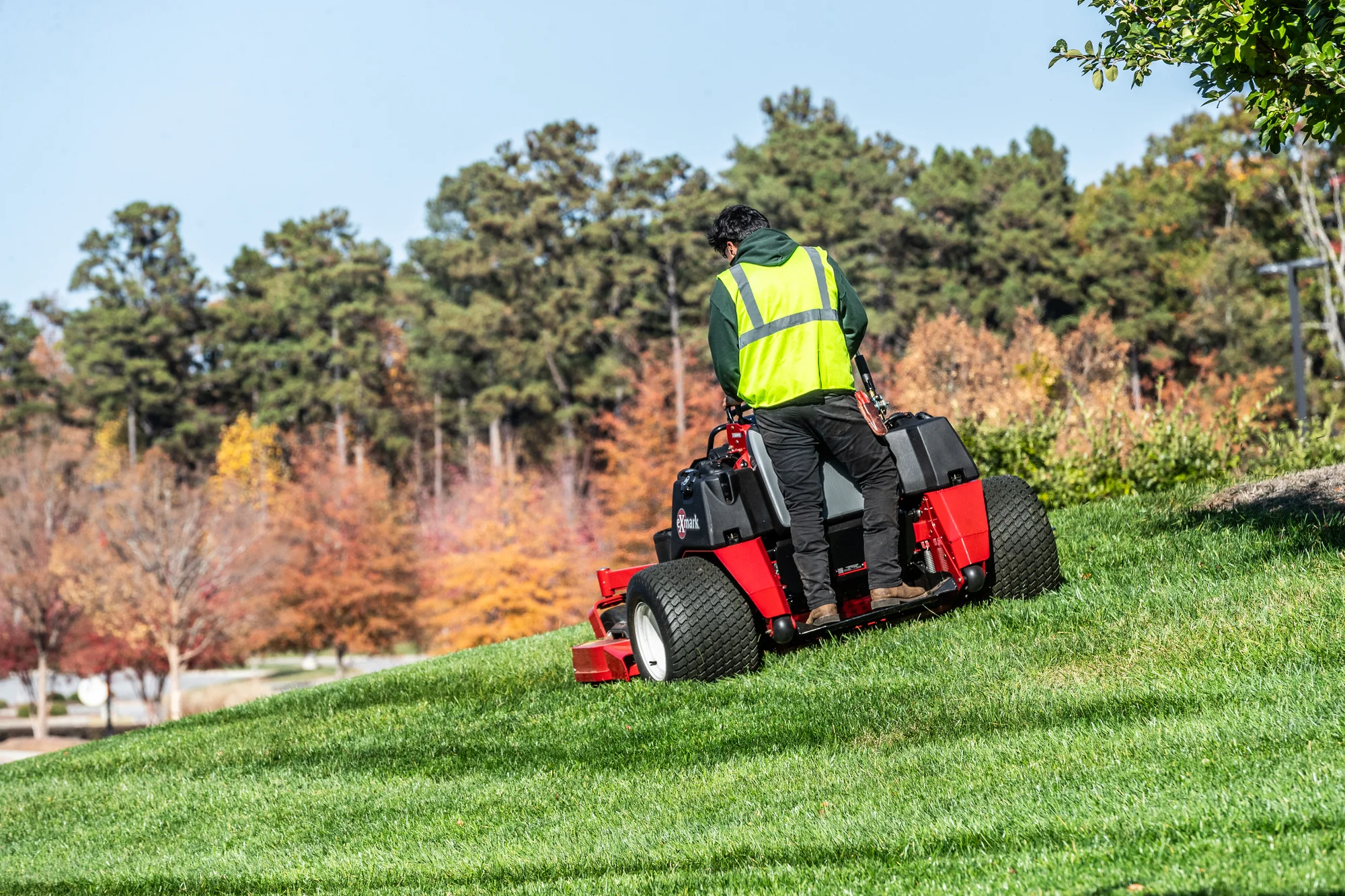 Exmark Vertex X Series Stand-On Lawn Mower VXX999EKA60600 Exmark Vertex X Series Stand On Lawn Mower Vxx999Eka60600 Back View Man With Mask Mowing Hill product image
