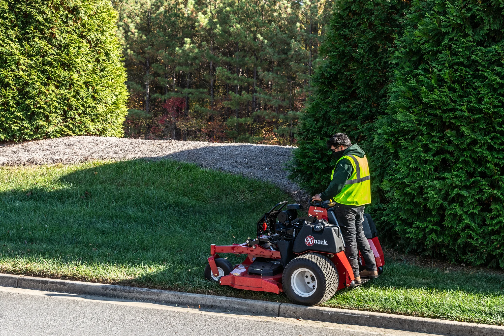 Exmark Vertex X Series Stand On Lawn Mower Vxx999Eka60600 Side View Man With Mask Mowing Near Road product image